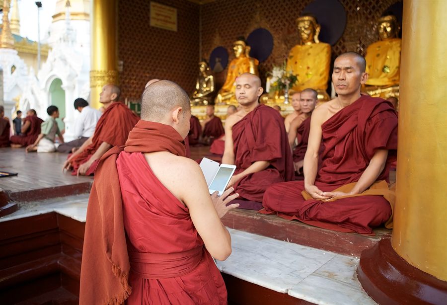 Buddhist monks in maroon robes seated in prayer inside a gilded shrine